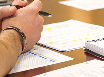 close up shot of a hand holding a pen with reports on the table.